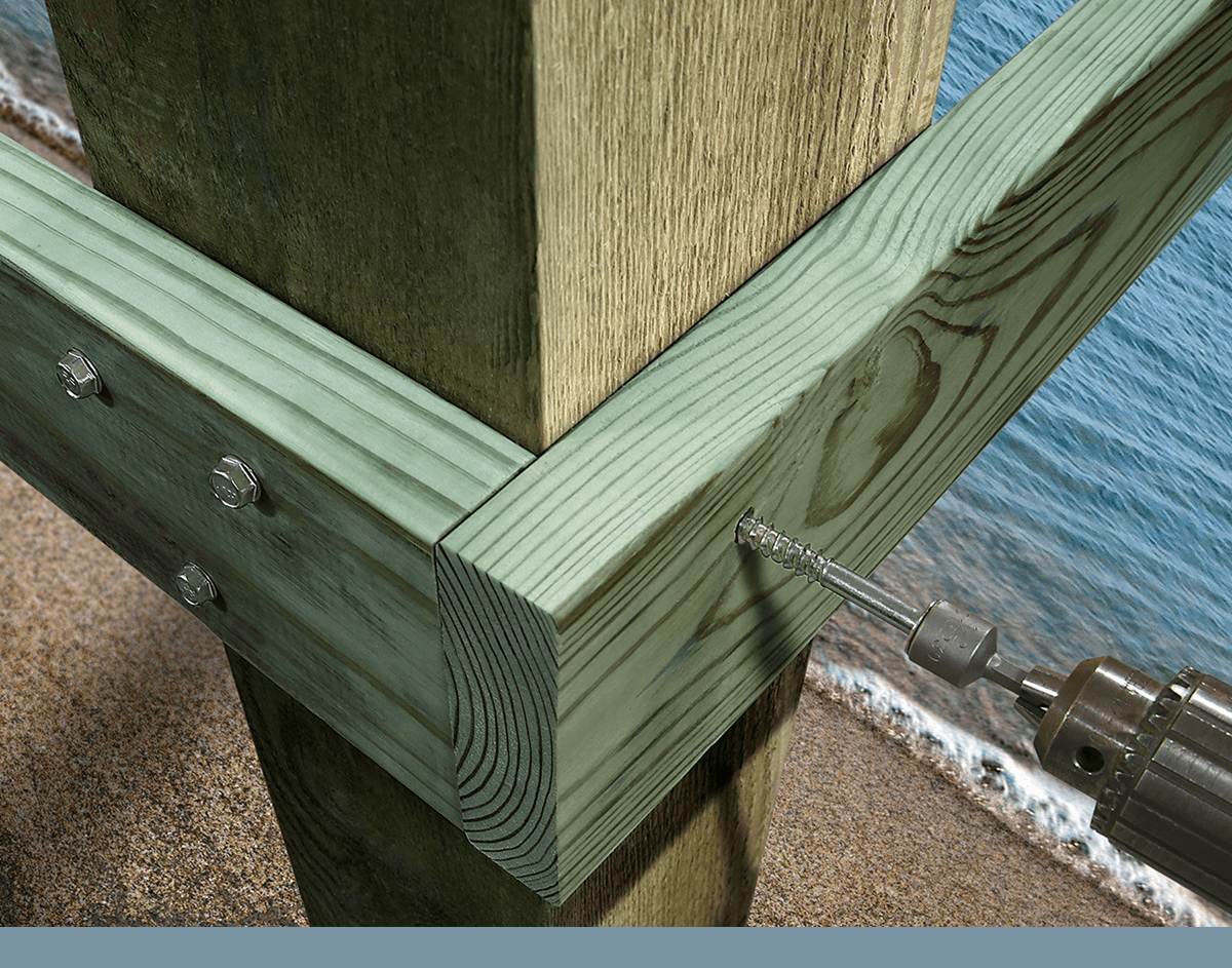 Simpson Strong-Tie fastener being driven into pressure-treated lumber for a coastal construction project using a power drill.